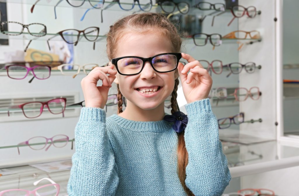 Happy girl at optometrist office trying on different glasses