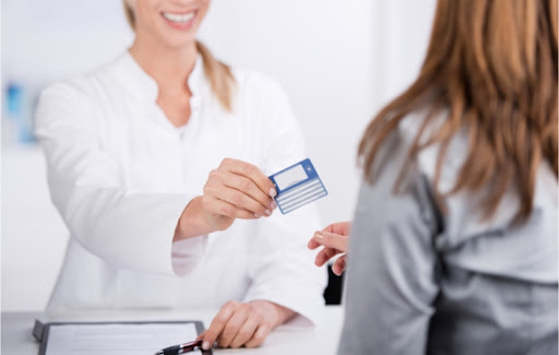 Smiling female optometrist holding out female patient's healthcare card in the process of returning it to her.
