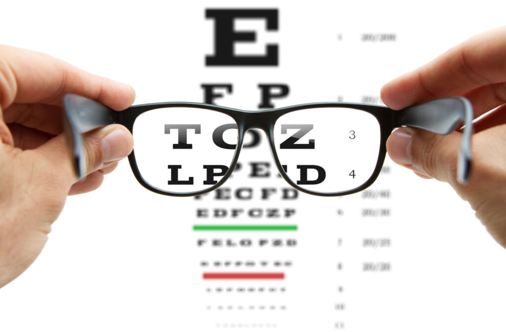 A pair of glasses being held out in front of a Snellen chart during an eye exam at an optometry office to determine a new prescription.