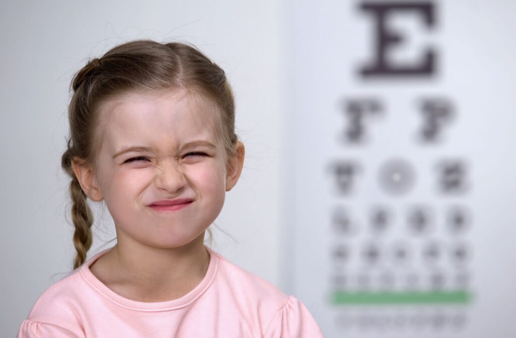 A young child squinting while looking at an eye chart during a myopia assessment.
