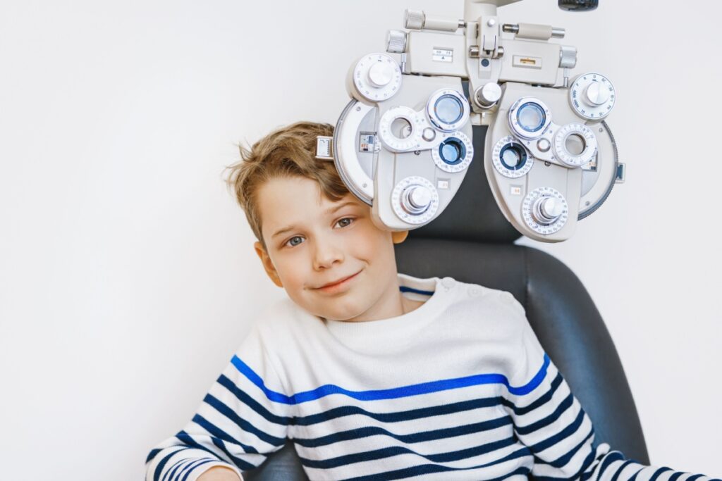 A young kid at an eye exam, sitting in the exam chair behind a phoropter.