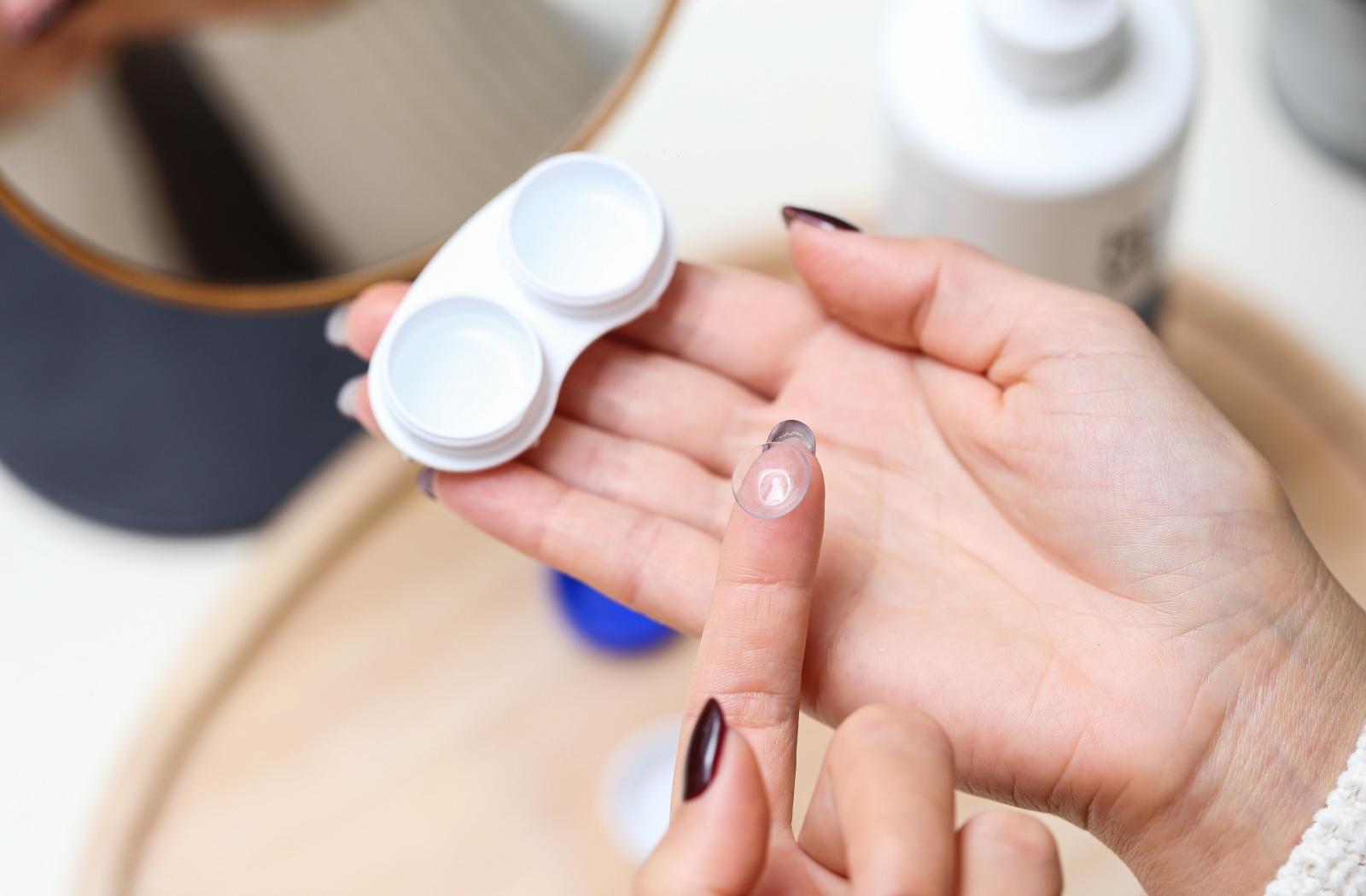 A person holding a contact lens on their finger on one hand and a contact lens case in the other hand.